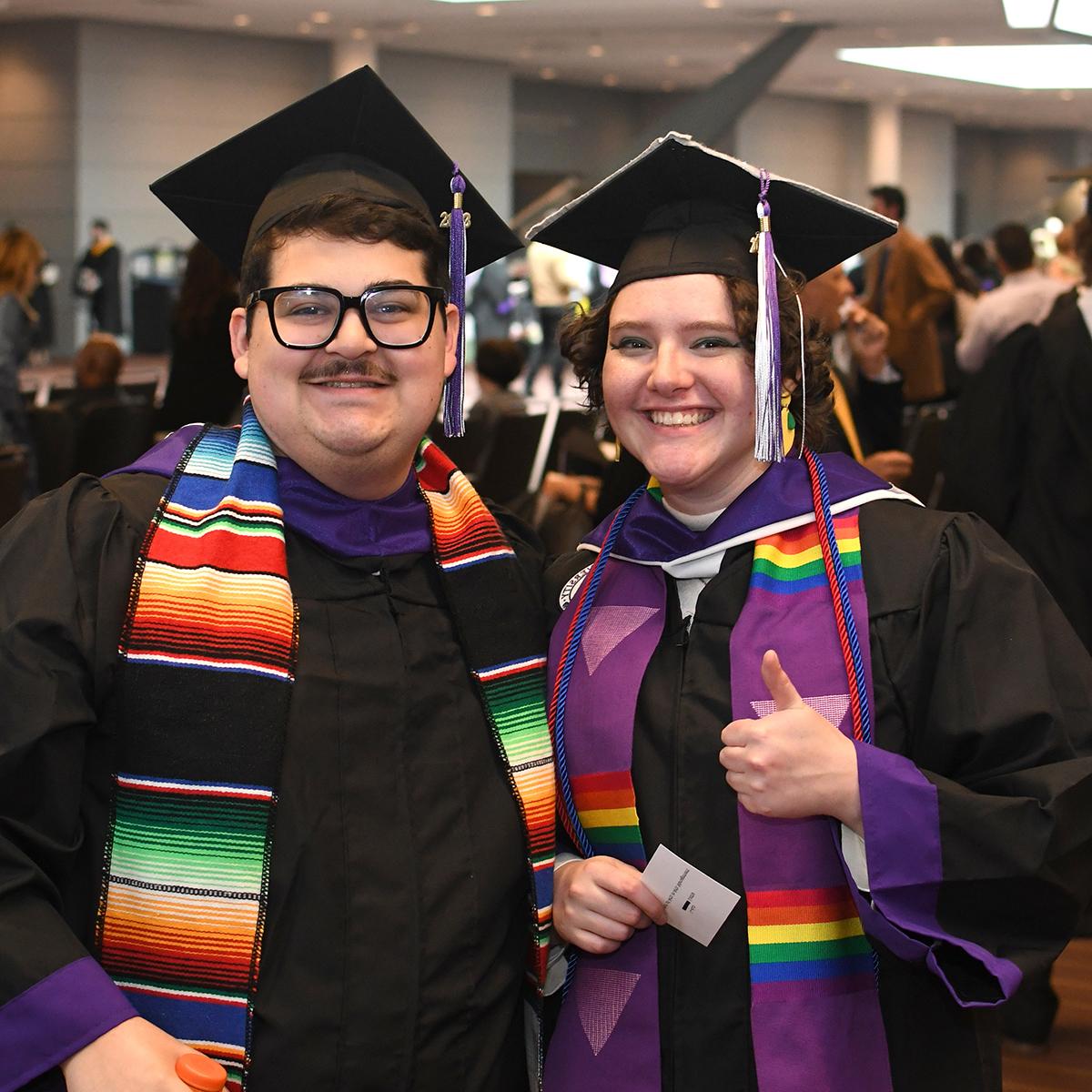 Two graduating students in caps and gowns pose for a photo, smiling